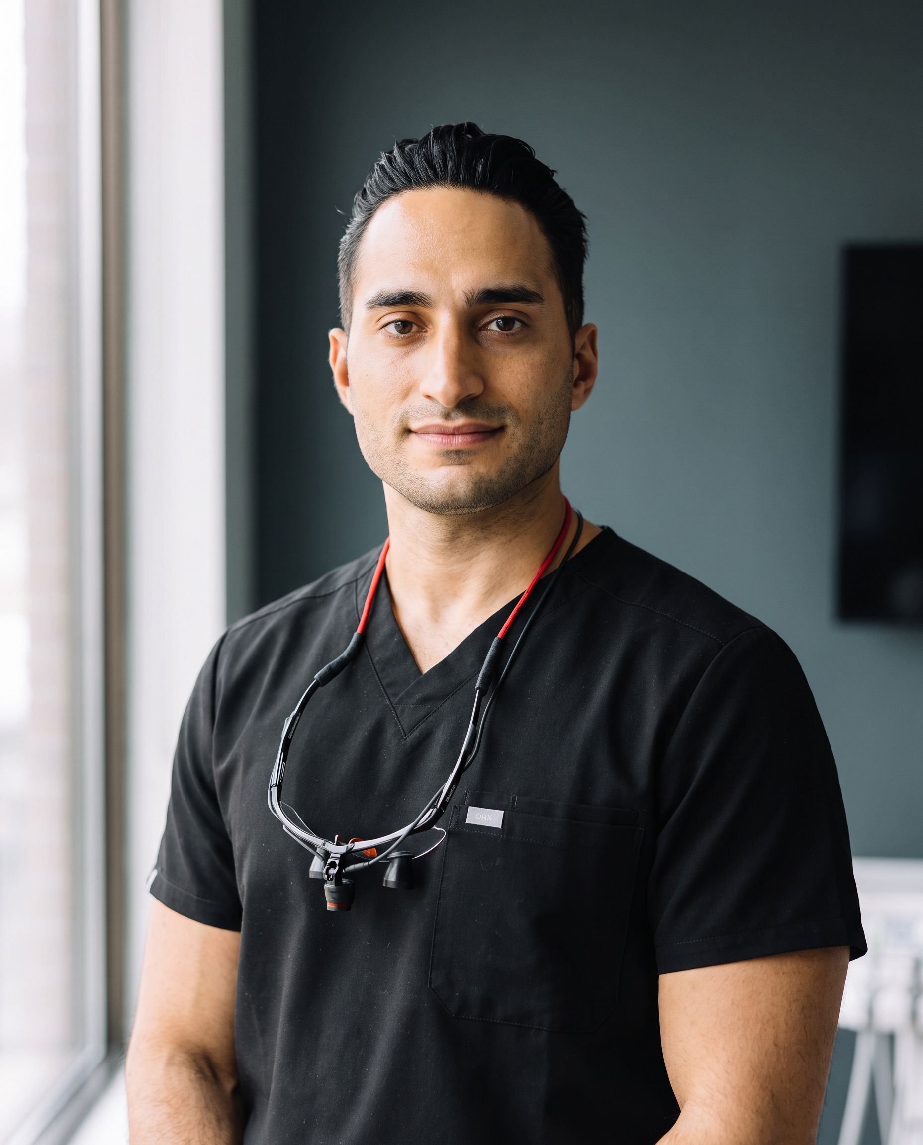 Portrait of Dr. Amir Moradian in black scrubs with loupes around his neck