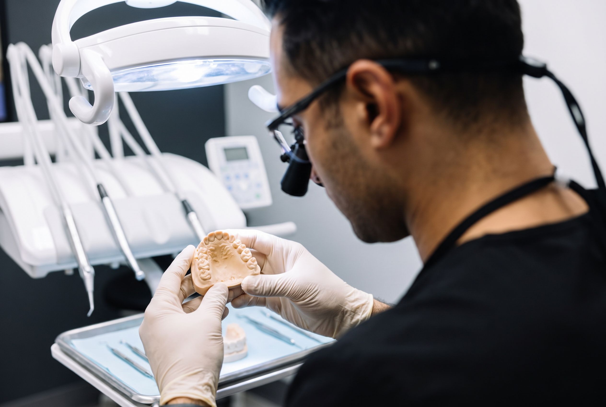 Dr. Moradian in loupes, holding a cast of an upper arch under the chair light